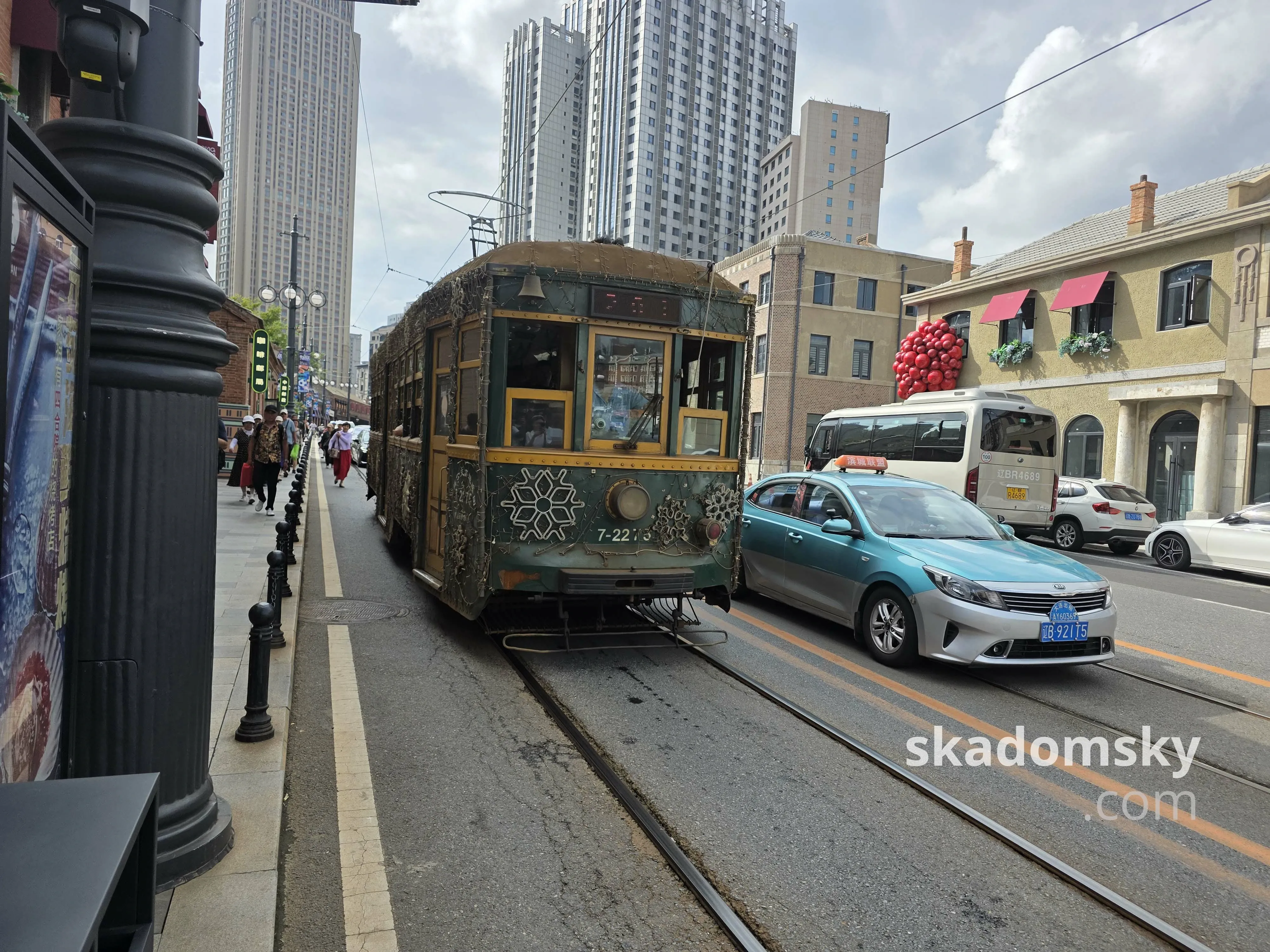 一辆绿色单节老式有轨电车朝向站台这边驶来。旁边有一辆蓝色的出租车。