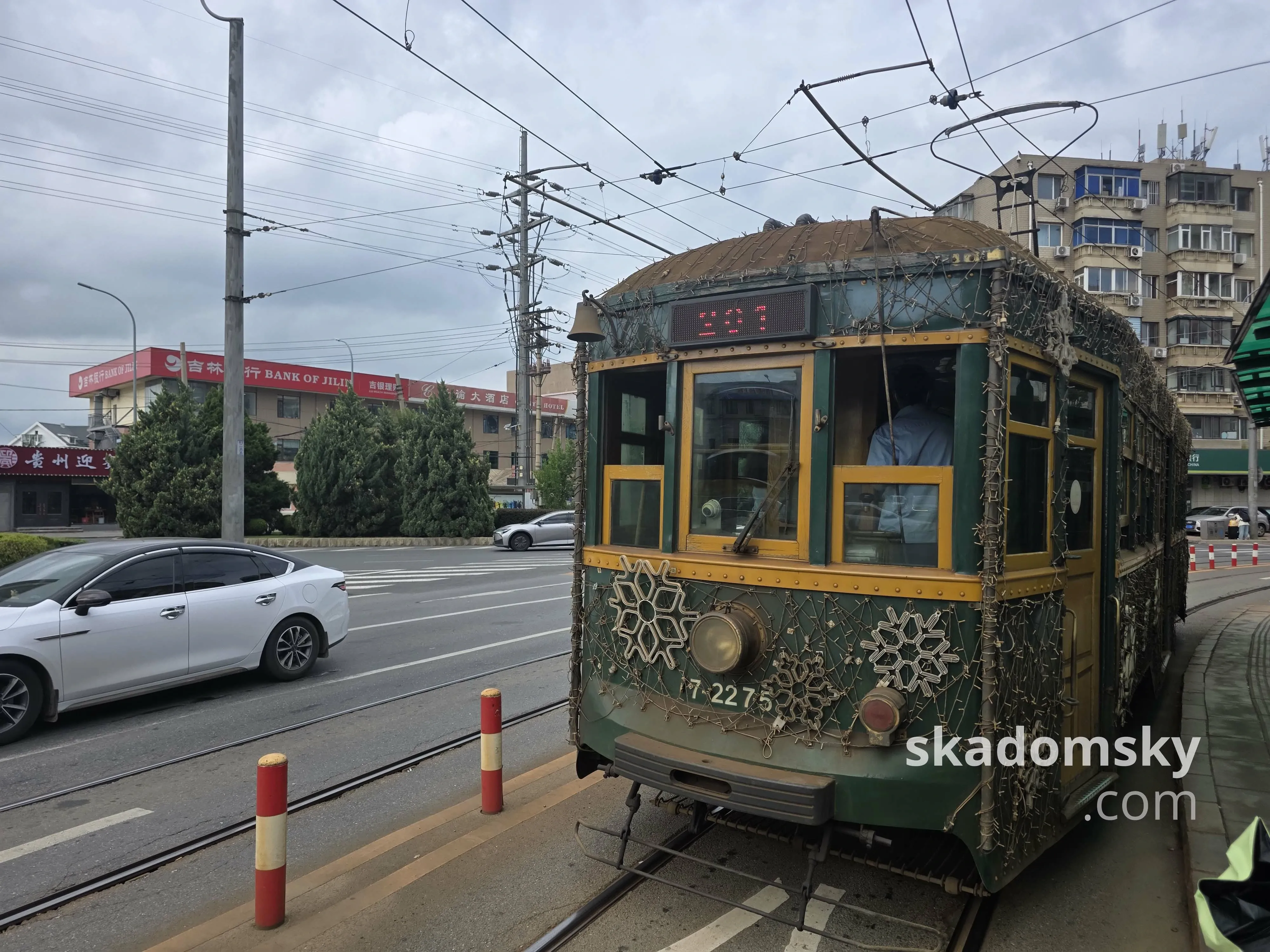 一节绿色的老式有轨电车停靠车站。旁边一辆白色轿车经过。