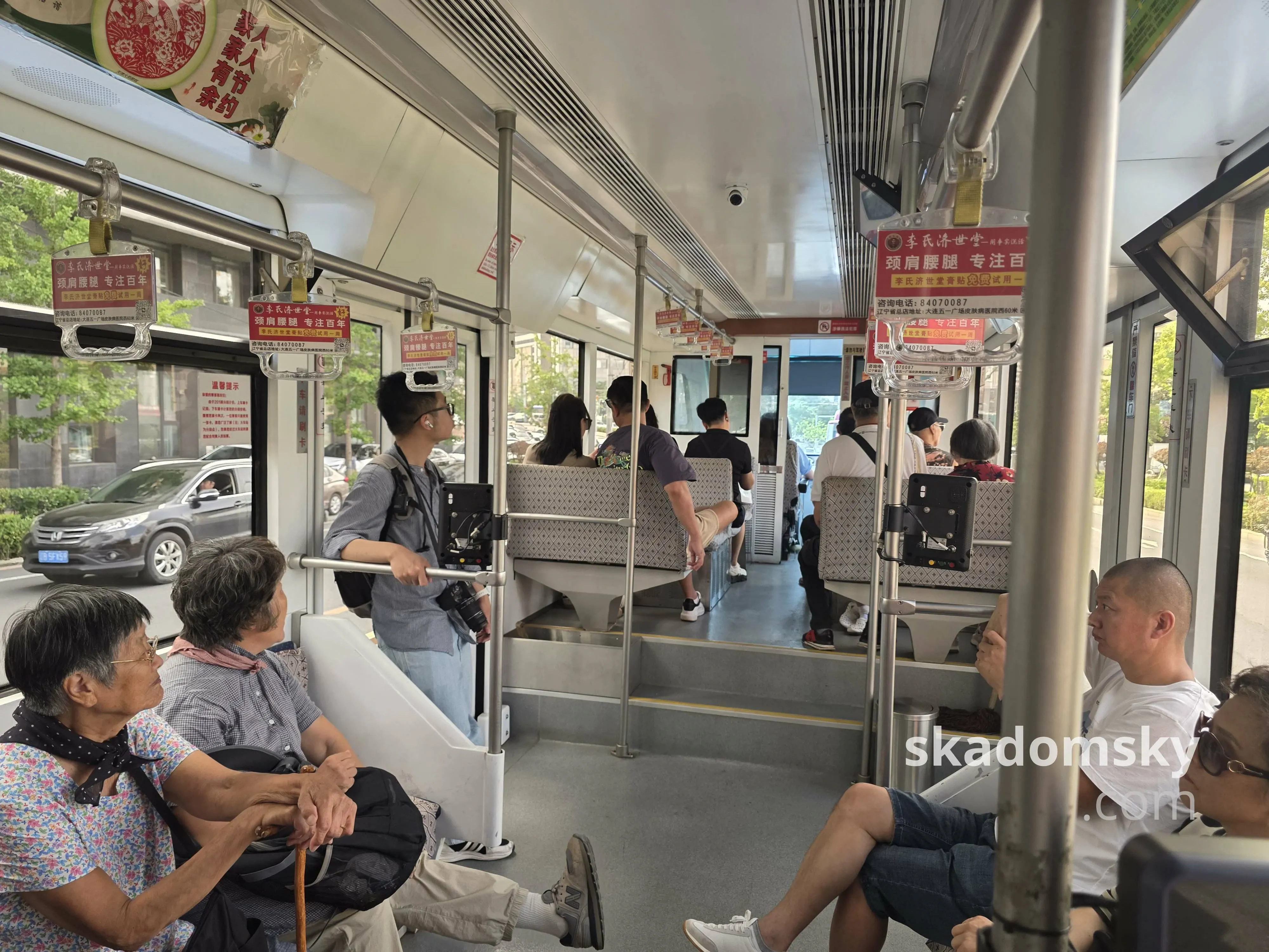 有轨电车车头车厢内部。不少老人坐在两侧的座位上,左侧车门处一个挂着相机的男人靠着栏杆。