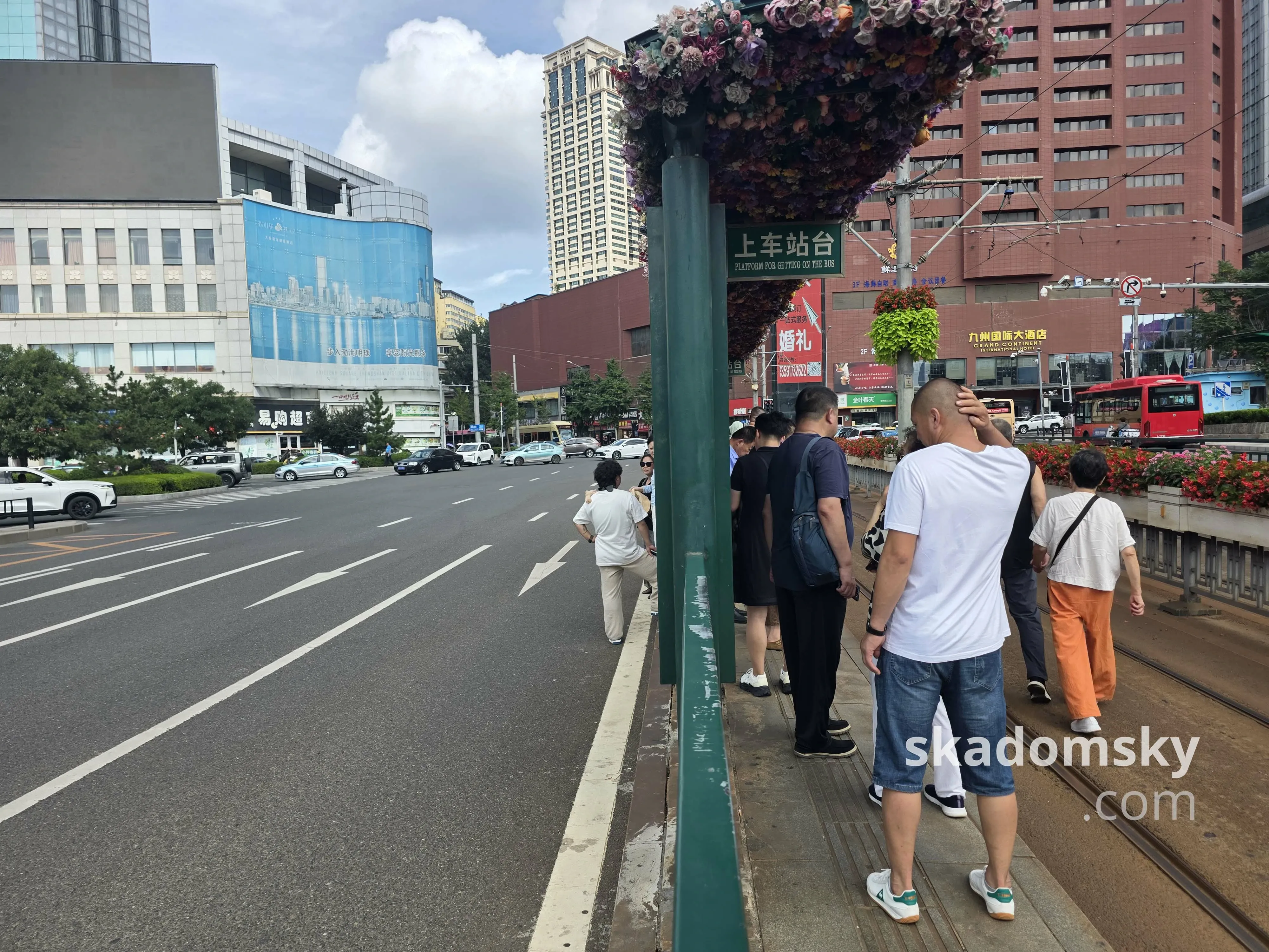 路中间有轨电车的上车站台,左侧是沥青马路,右侧是轨道区域。乘客在站台上等待。